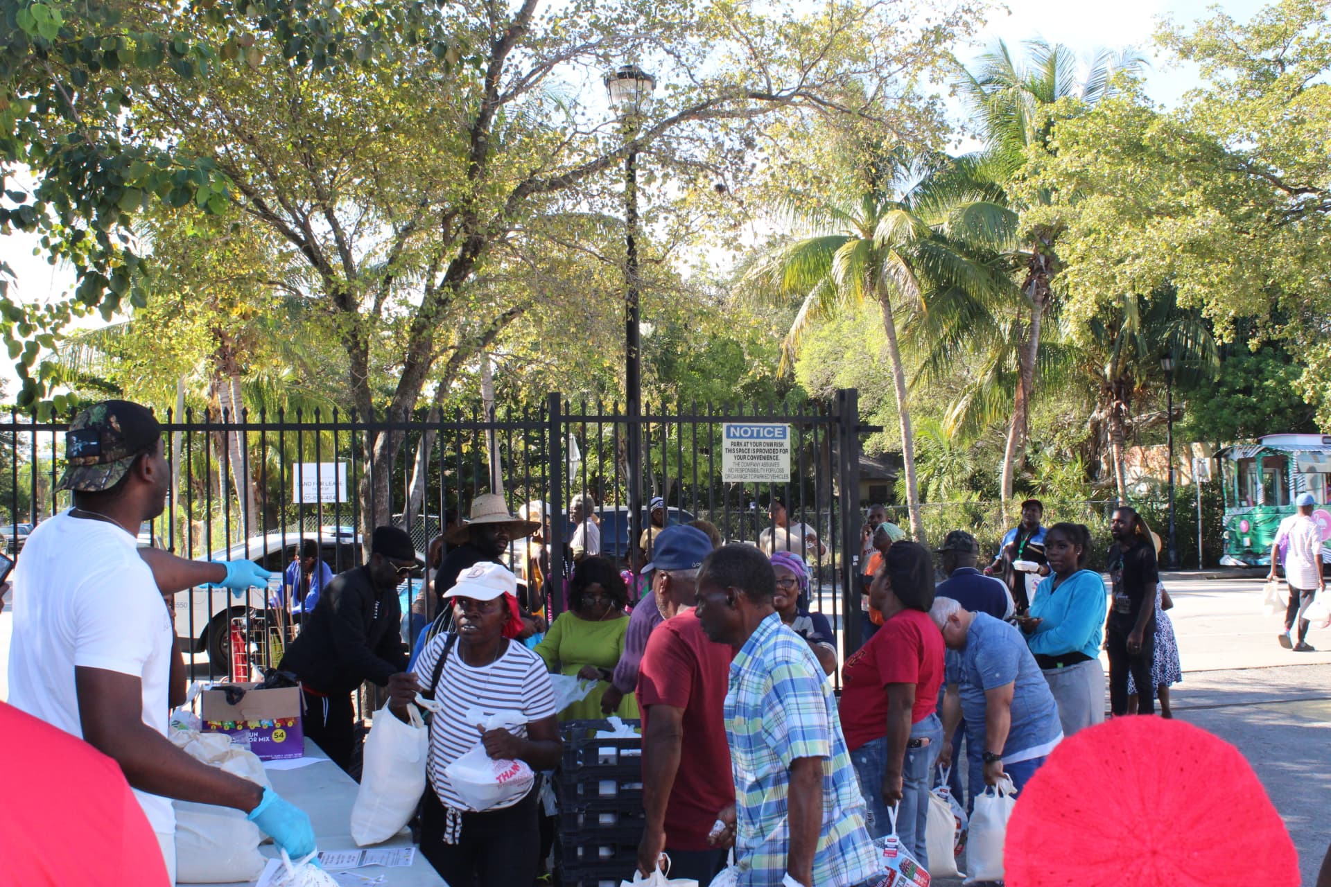 Volunteers at a table hand bags of groceries to neighbors waiting in line at an outdoor TAPARI food distribution.